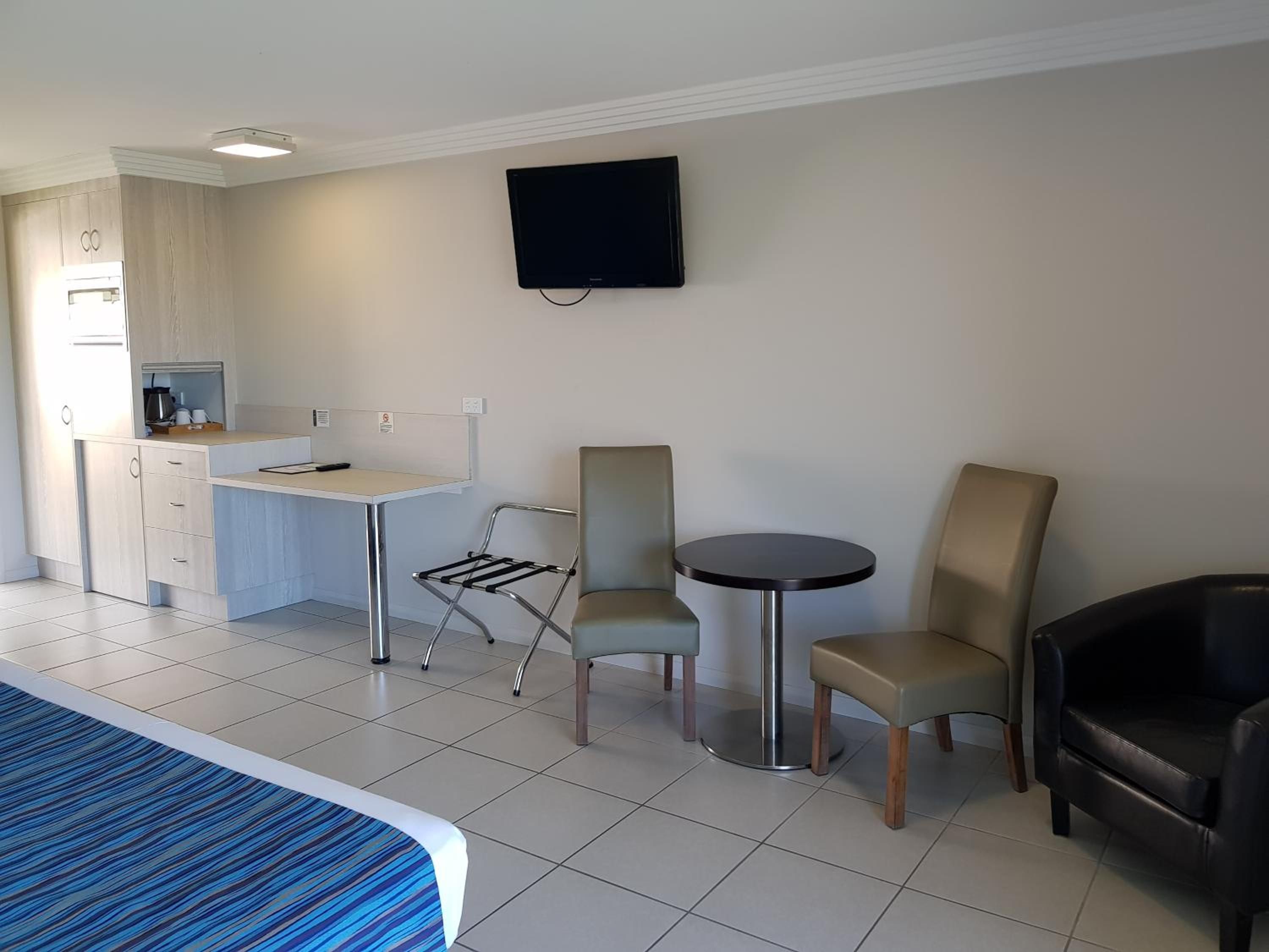 A hotel room with a bed, a desk, a chair, a small table, and a TV mounted on the wall.