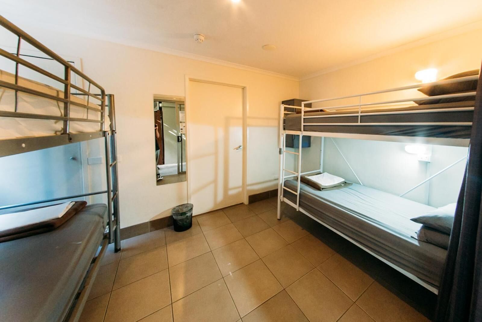 Een slaapzaal met stapelbedden, een kleine prullenbak en een deur naar een andere kamer.
