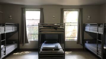 Un dormitorio con literas, dos ventanas con cortinas y un escritorio pequeño.