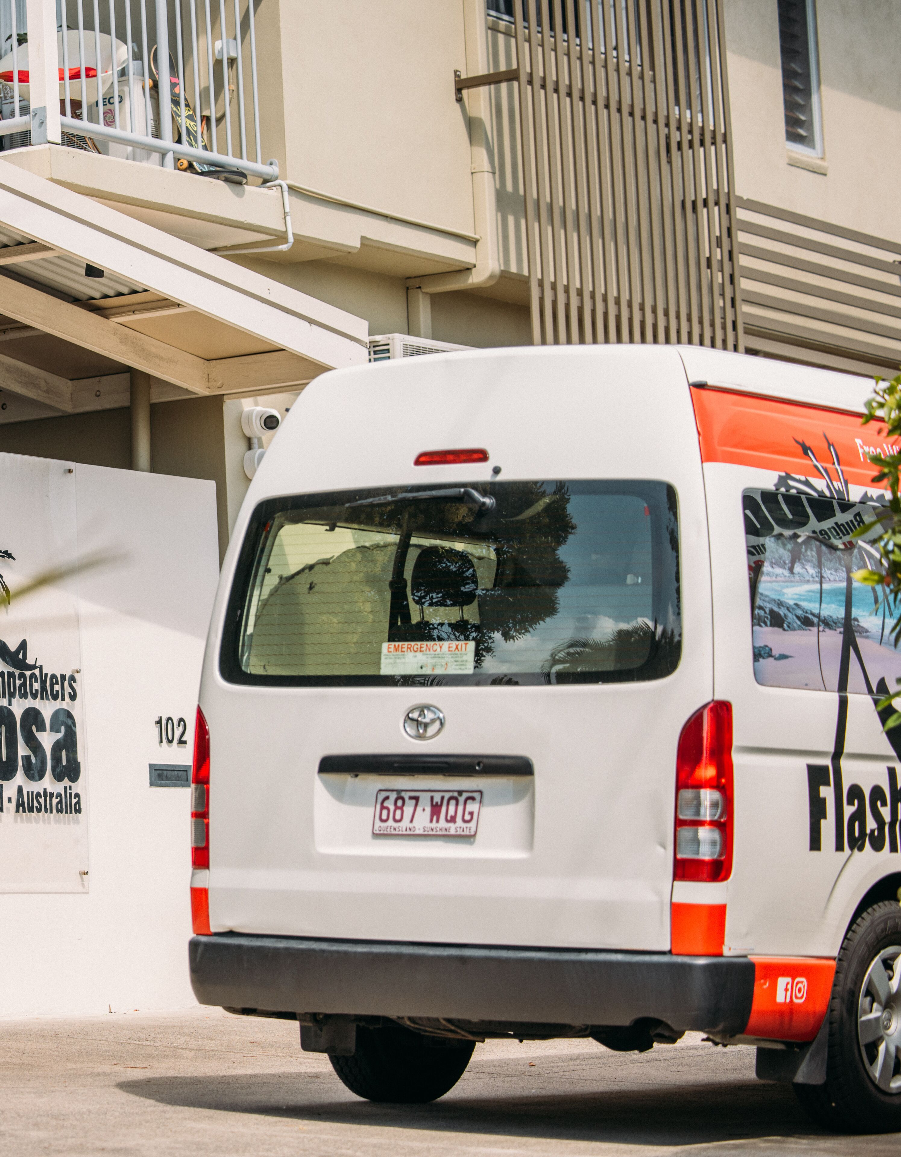 A white van parked in front of a building with a sign that reads "Emergency Exit".