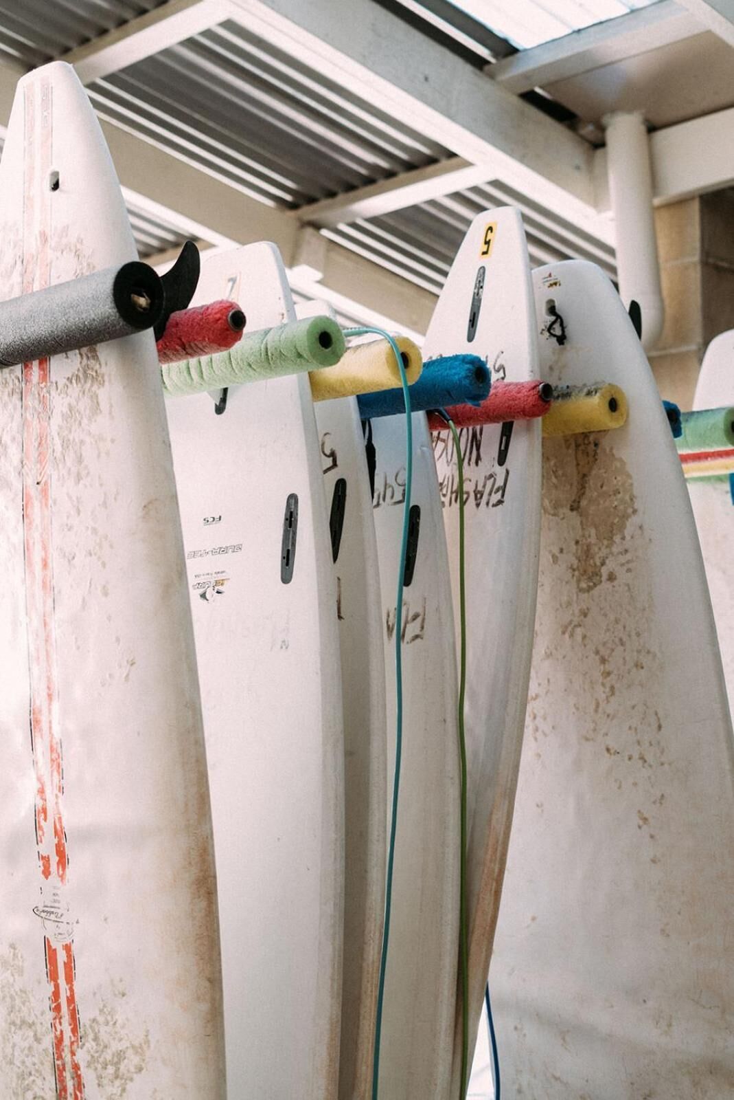 Surfboards with colored tape and numbers, likely for identification, in a storage area with metal racks.