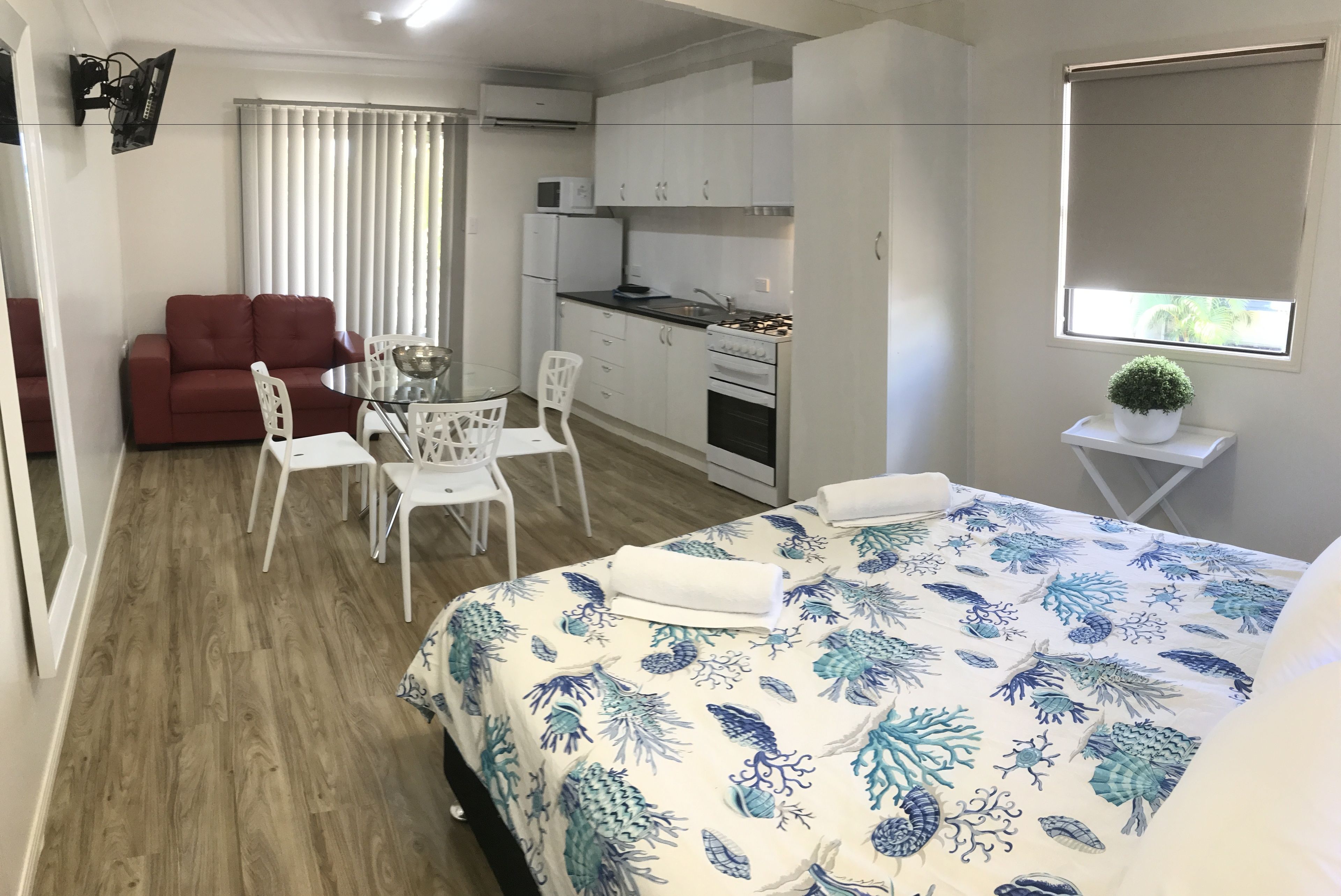 Habitación compacta con cama, una kitchenette pequeña, un sofá rojo y un comedor.