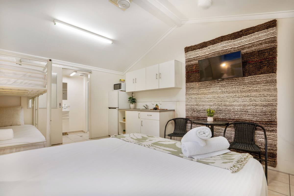 Een hotelkamer met een bed, een bureau, een stoel, een aan de muur bevestigde televisie en een kitchenette.