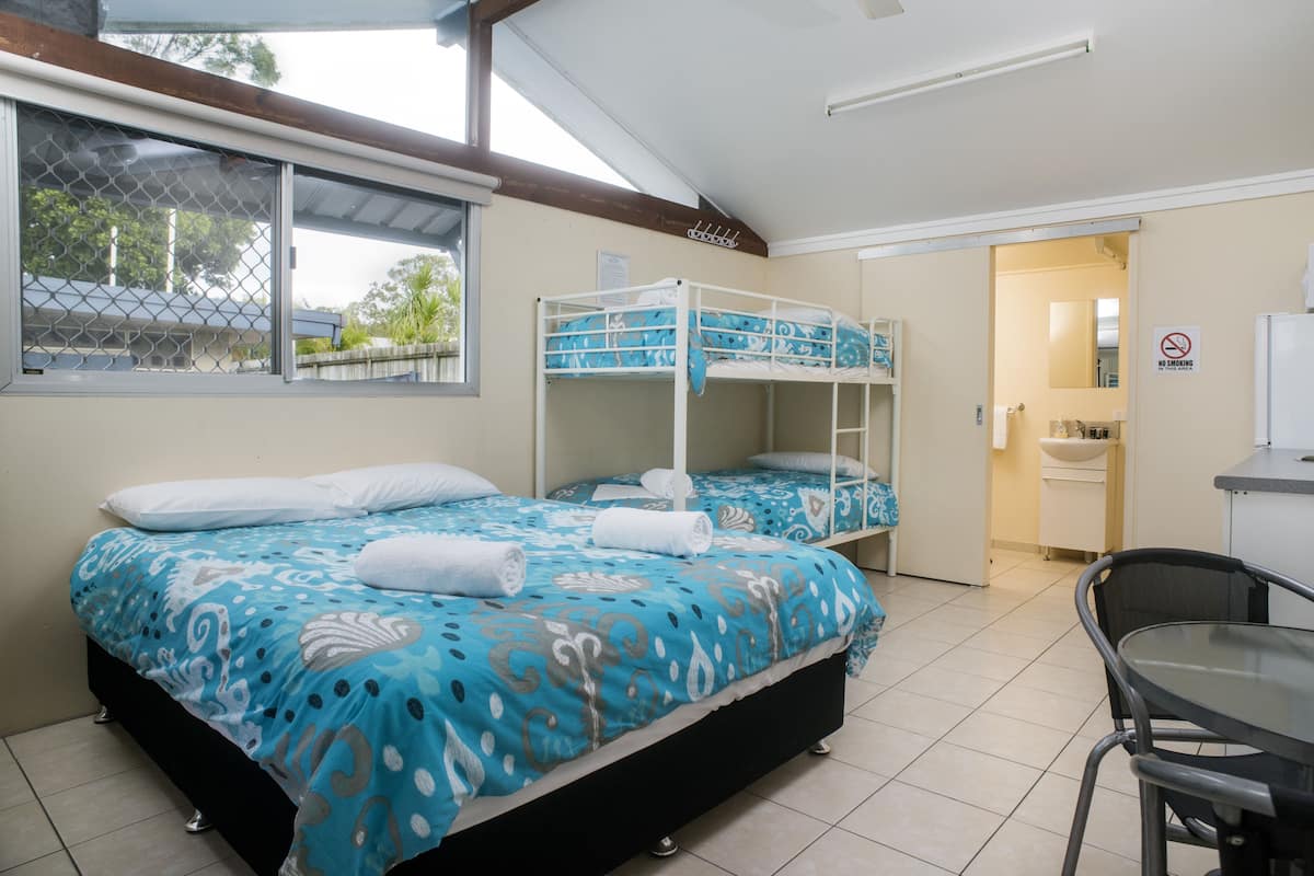 Een stapelbed met een bedsprei met patroon, een eettafel en een badkamer zichtbaar door een geopende deur.