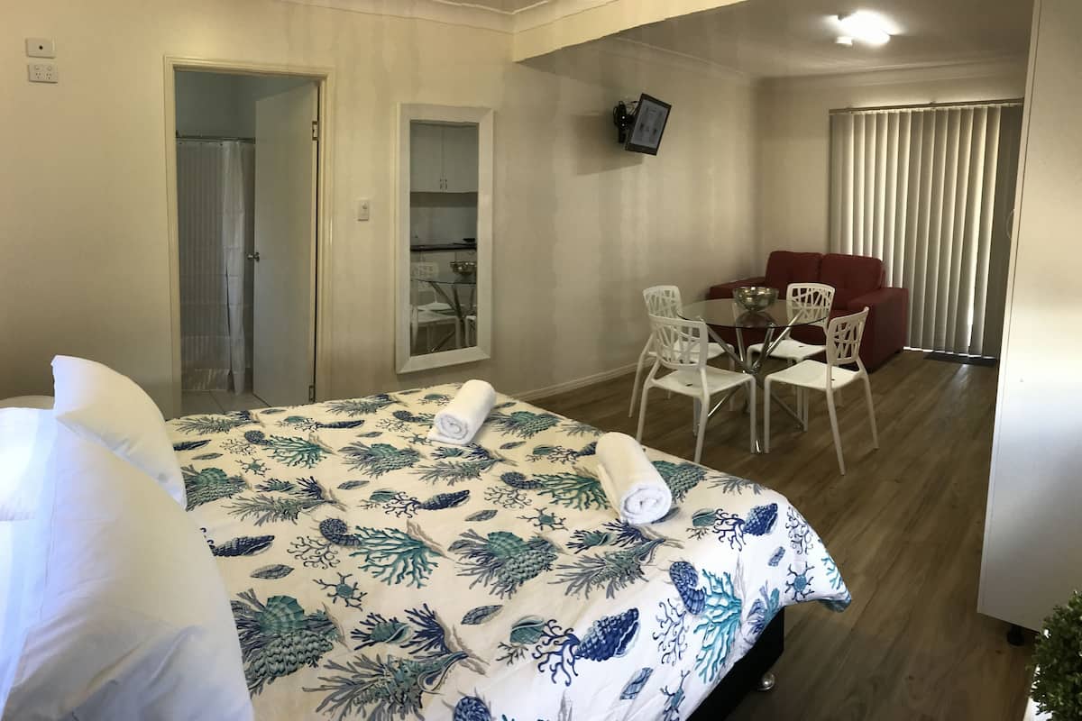 Een hotelkamer met een bed, een zithoek met een tafel en stoelen, een rode bank en een aan de muur bevestigde televisie.