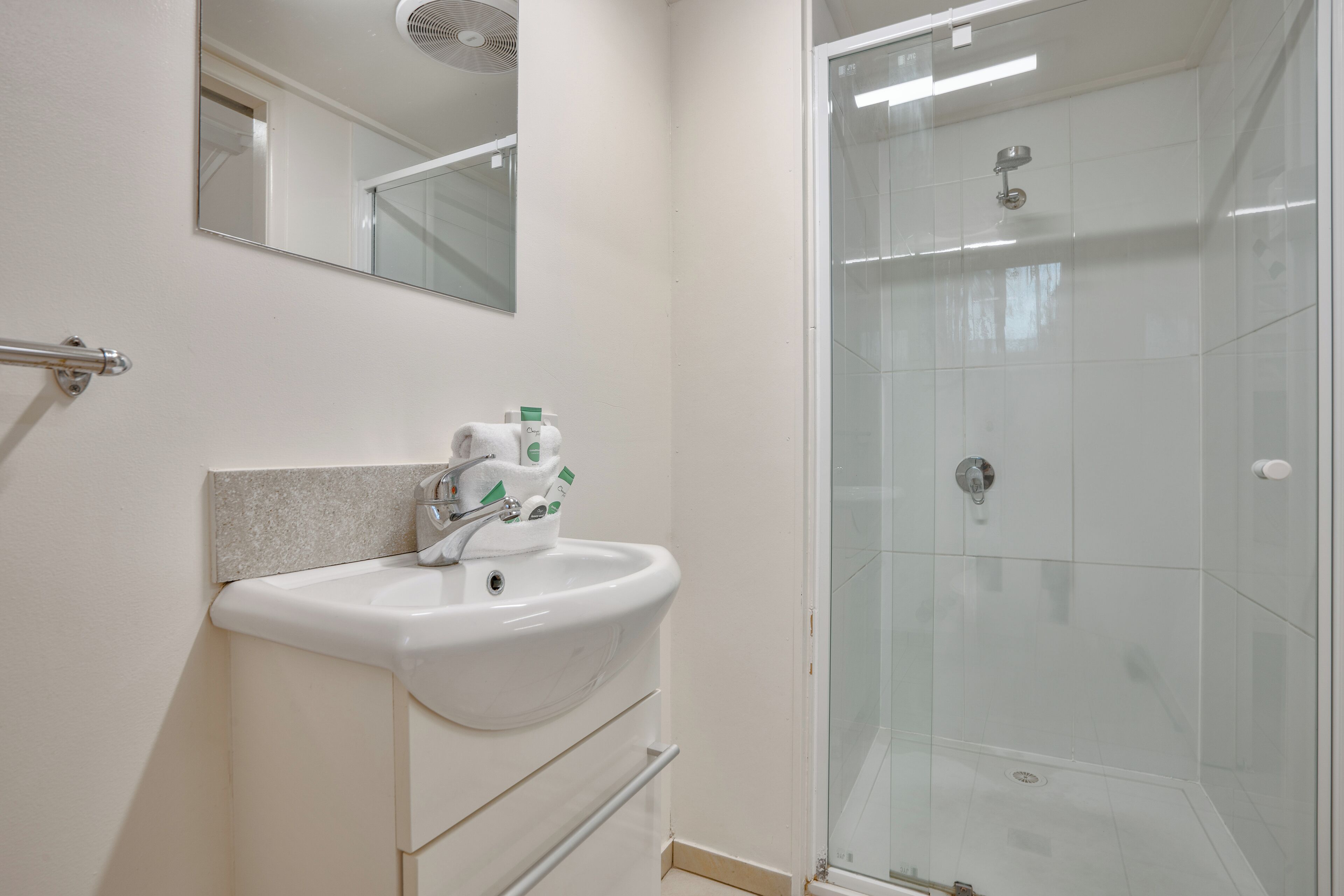 Een badkamer met een wit wastafelmeubel, spiegel en een douchecabine.