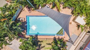 Vista aérea de una piscina rodeada de palmeras y una zona con sombra.