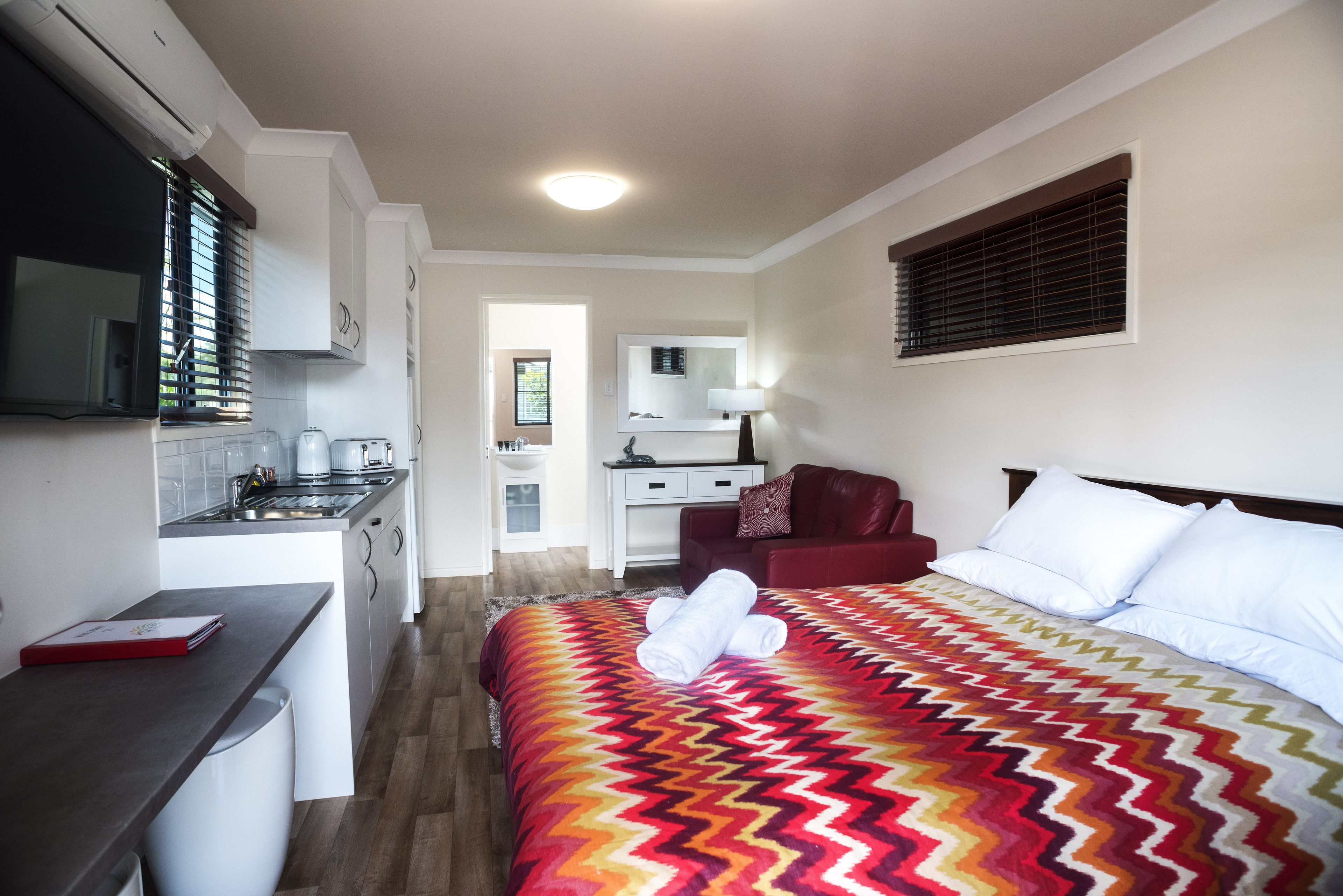 Habitació d'hotel amb llit, escriptori, petita cuina i bany.
