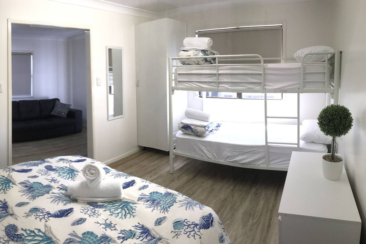 Hotelkamer met een stapelbed, een bank in de aangrenzende kamer, een potplant en een nachtkastje.