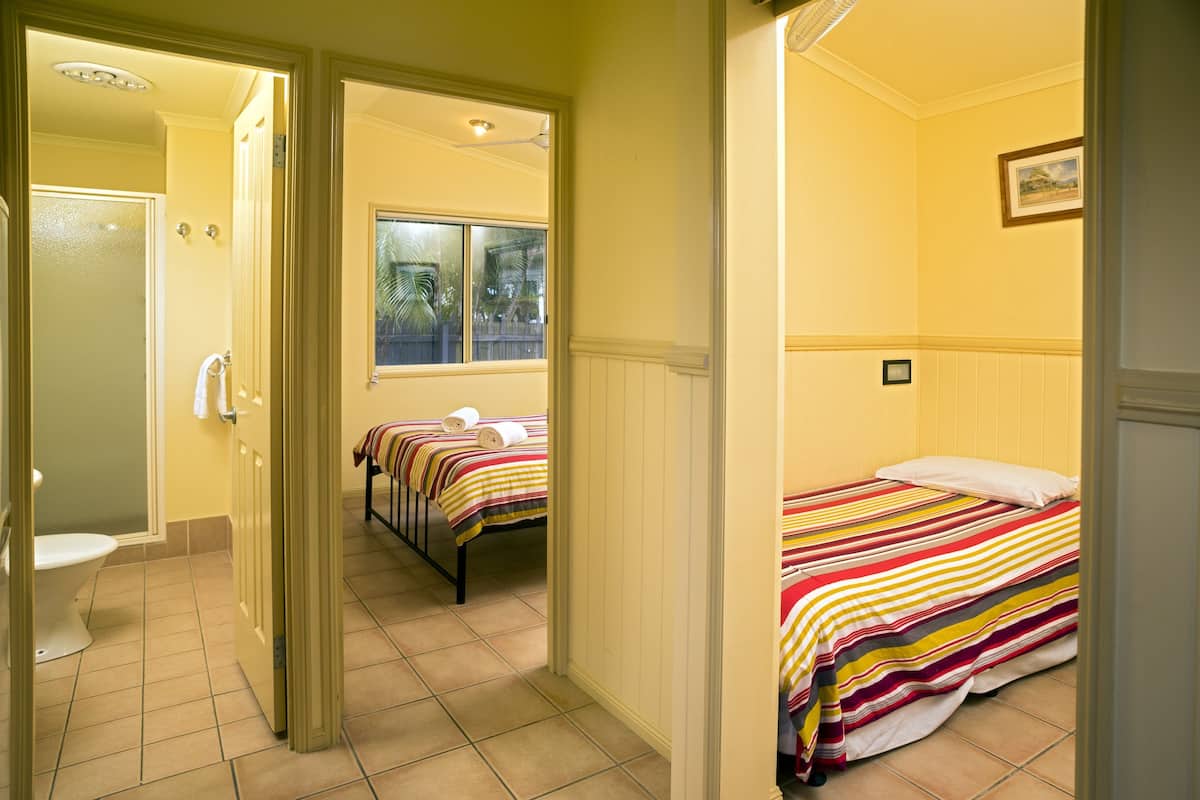 Een hotelkamer met een badkamer, een bed met een gestreept dekbed en een raam met uitzicht op palmbomen.