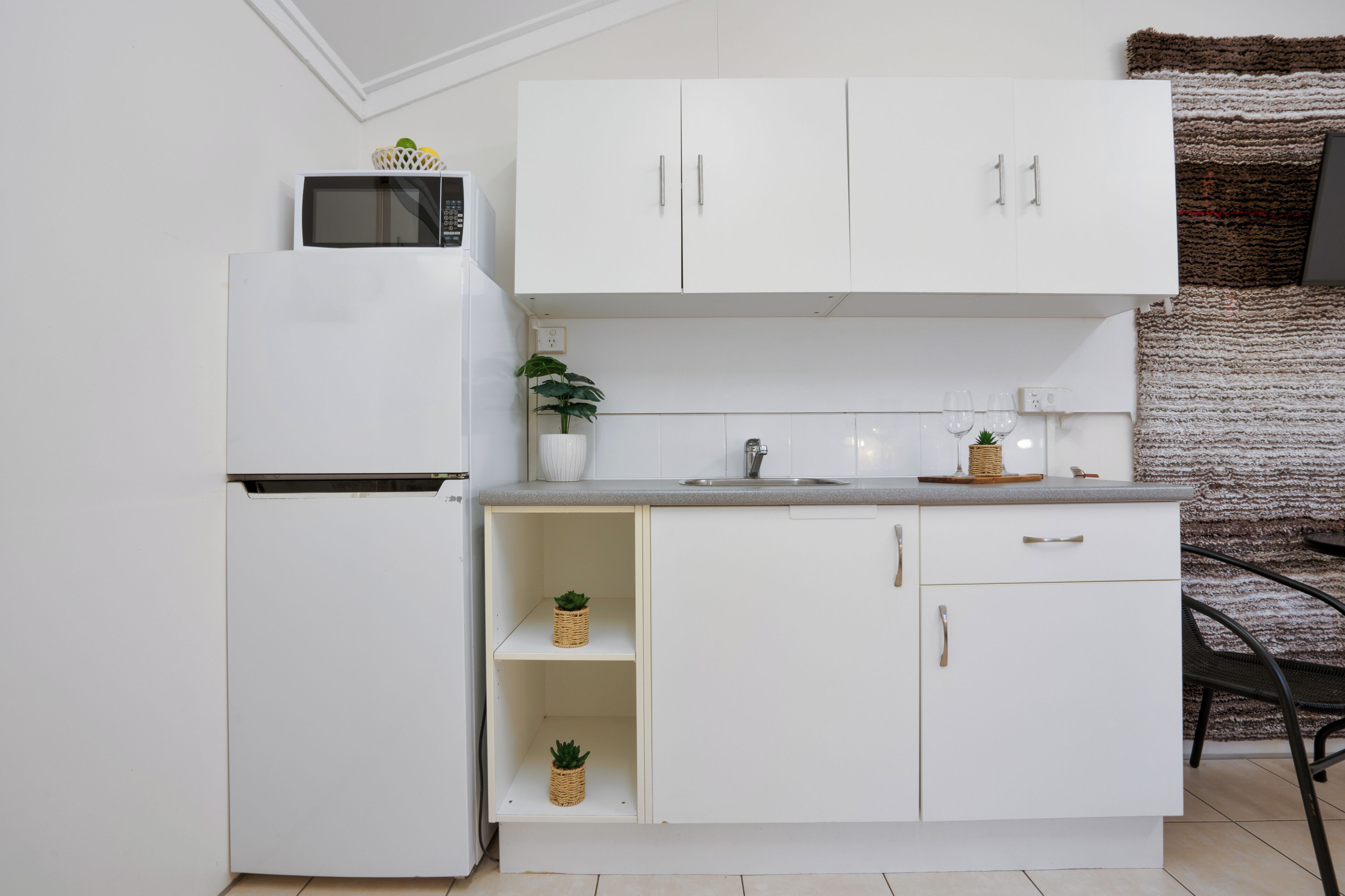 Une cuisine compacte avec des meubles blancs, un four à micro-ondes, un évier et une petite plante en pot.