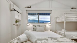 Un dormitorio con literas, una ventana con vistas, una cama con colcha estampada y un armario blanco.
