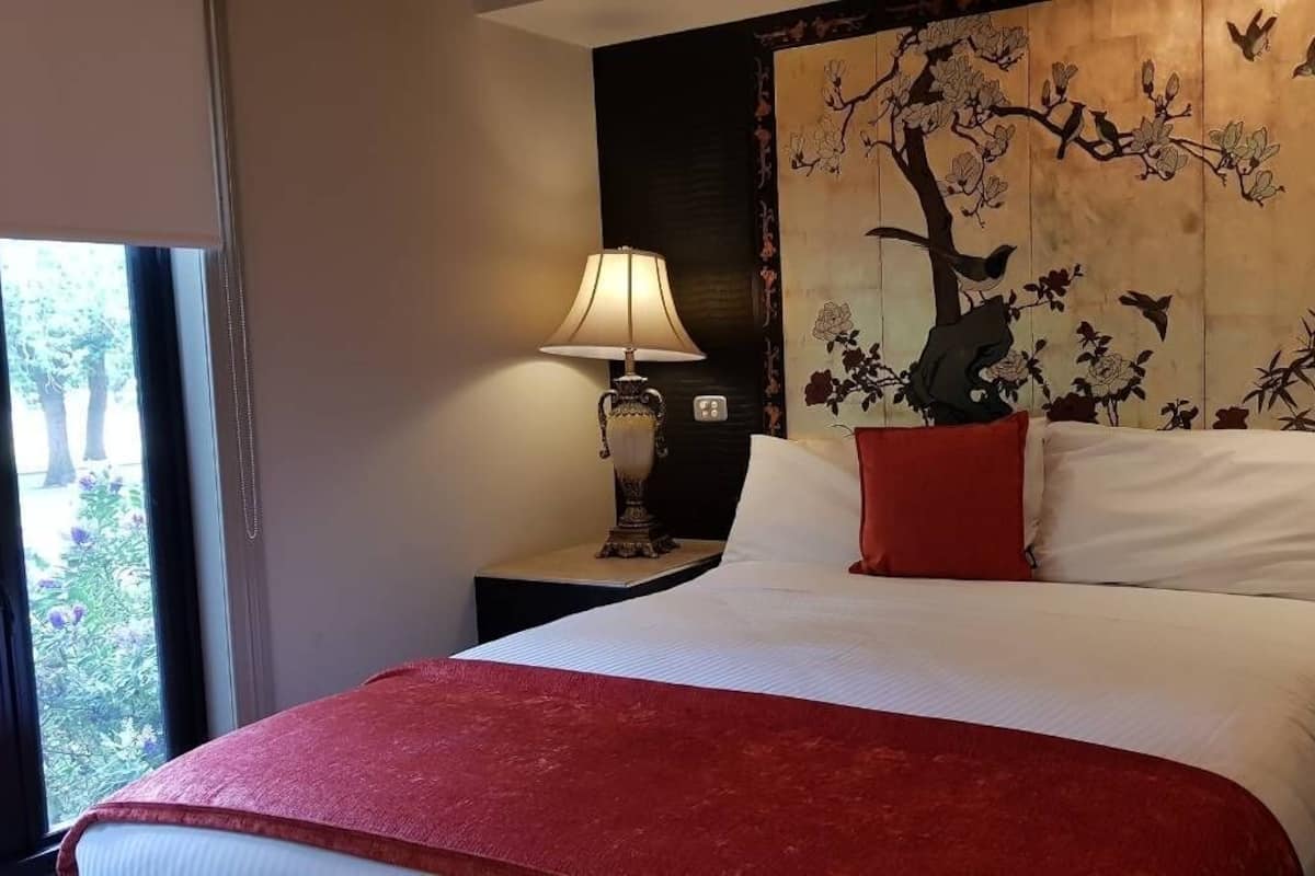 A hotel room with a bed, red throw, two nightstands with lamps, and a large wall mural.