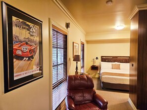 Una habitación de hotel con una cama, un sillón de cuero, una mesita de noche con lámpara y un cartel enmarcado en la pared.