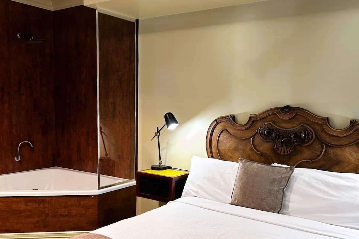 A hotel room with a large bed, a wooden headboard, a nightstand with a lamp, and a wooden wardrobe.