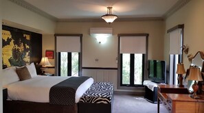 A hotel room with a large bed, a desk with a television, and a window with a view of trees. - The Camperdown Mill - South West Victoria (Camperdown)