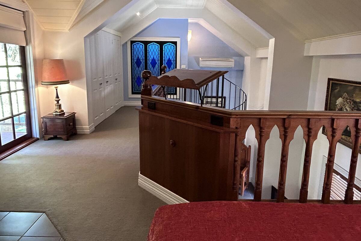 A spacious attic bedroom with a large window, a wooden staircase, and a view of the outside.