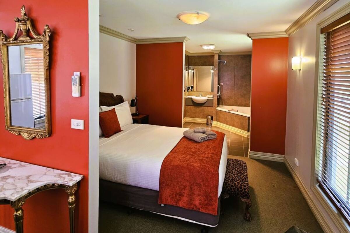 A hotel room with a bed, a vanity with a mirror, and a bathroom visible through an open door.