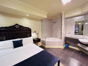 A hotel room with a bed, a nightstand, a desk lamp, a large mirror, a bathtub, and a sink. - The Camperdown Mill - South West Victoria (Camperdown)