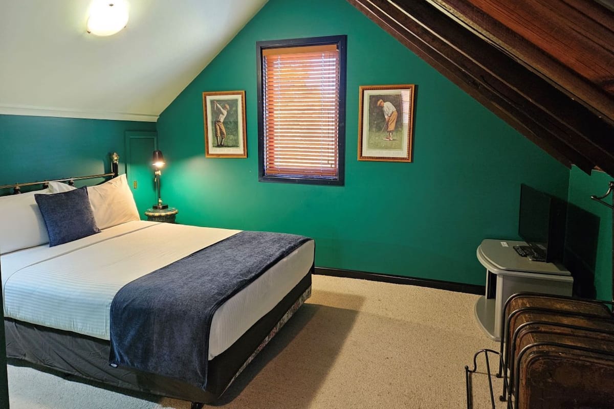 A bedroom with a bed, a desk, and a window with blinds.