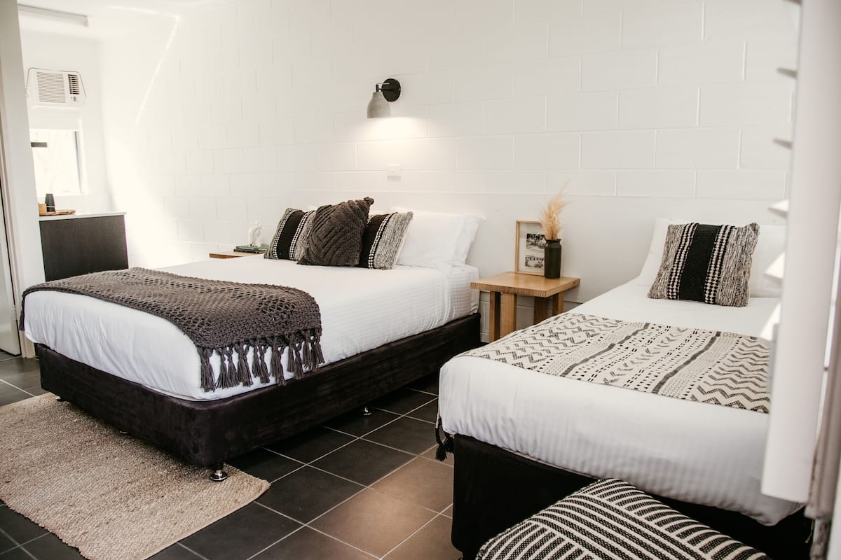 A hotel room with two beds, a small bedside table, a nightstand, and a wall-mounted lamp.