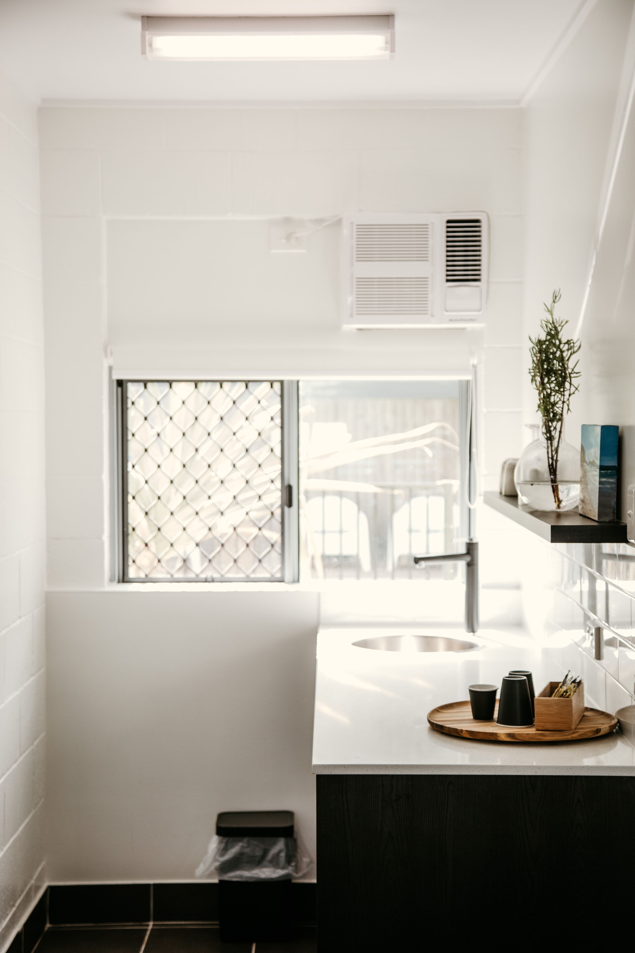 Un baño moderno con ventana, lavabo y un pequeño cubo de basura.