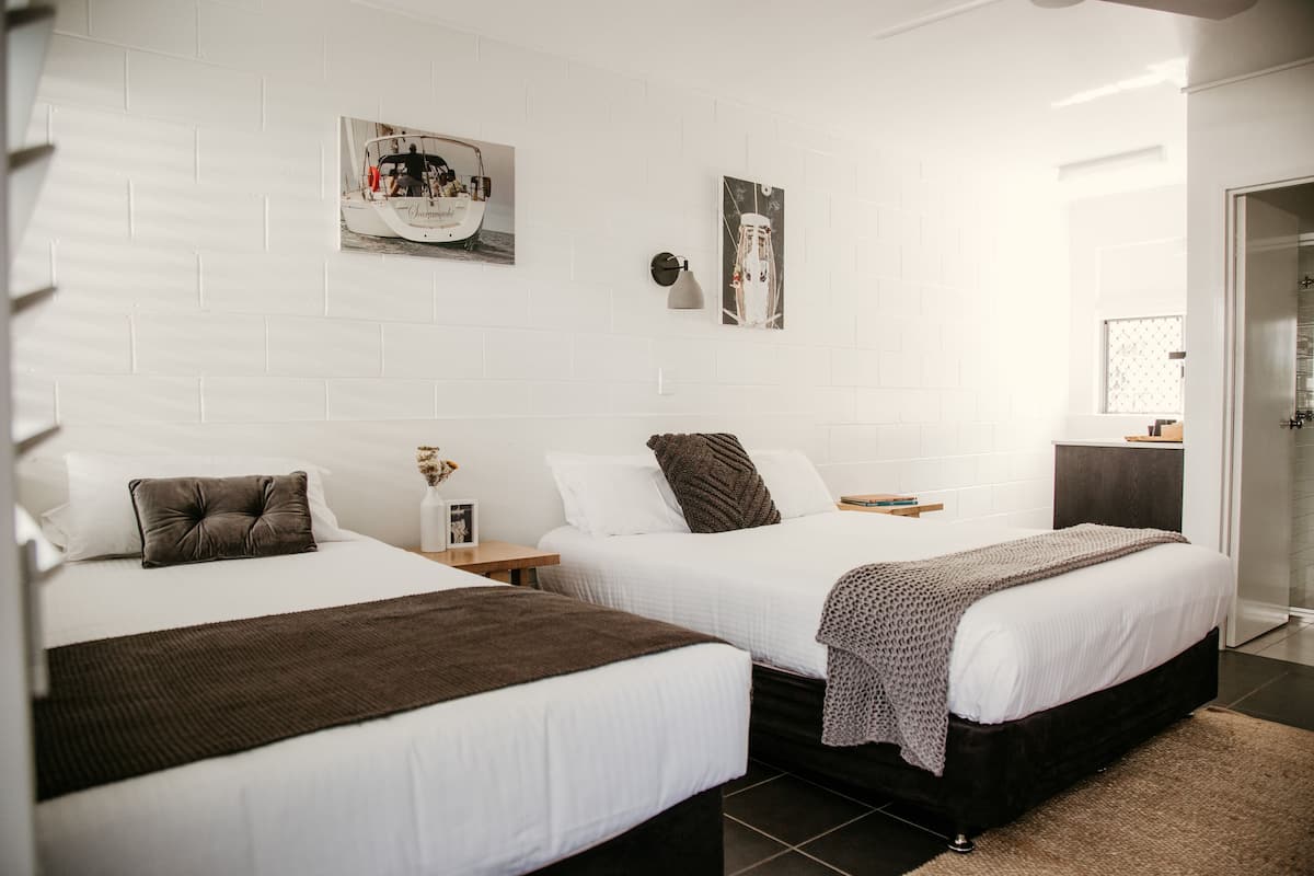 A hotel room with two beds, white walls, and a large window.