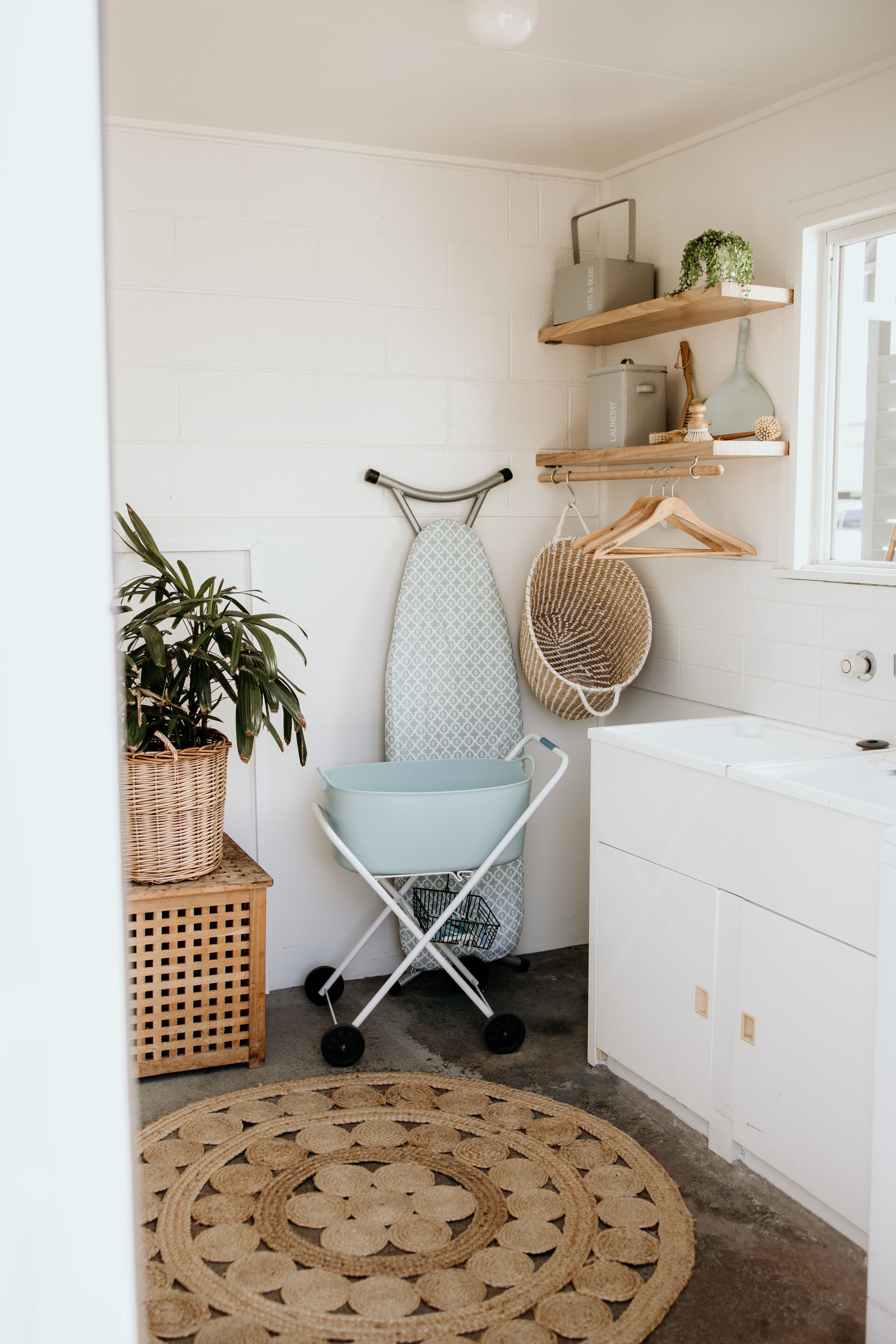 A bathroom with a white sink, a hanging laundry basket, a wicker basket, and a round woven rug.