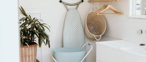 A bathroom with a white sink, a hanging laundry basket, a wicker basket, and a round woven rug.