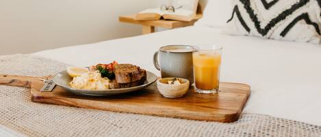 A neatly made breakfast on a wooden tray with a plate of food, a mug, and a glass of orange juice on a bed in a hotel room.