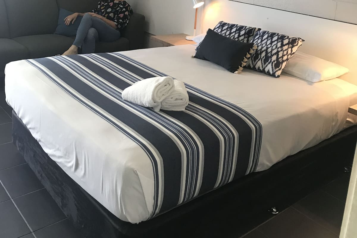 A hotel room with a bed, a sofa, a lamp, and a framed picture on the wall.