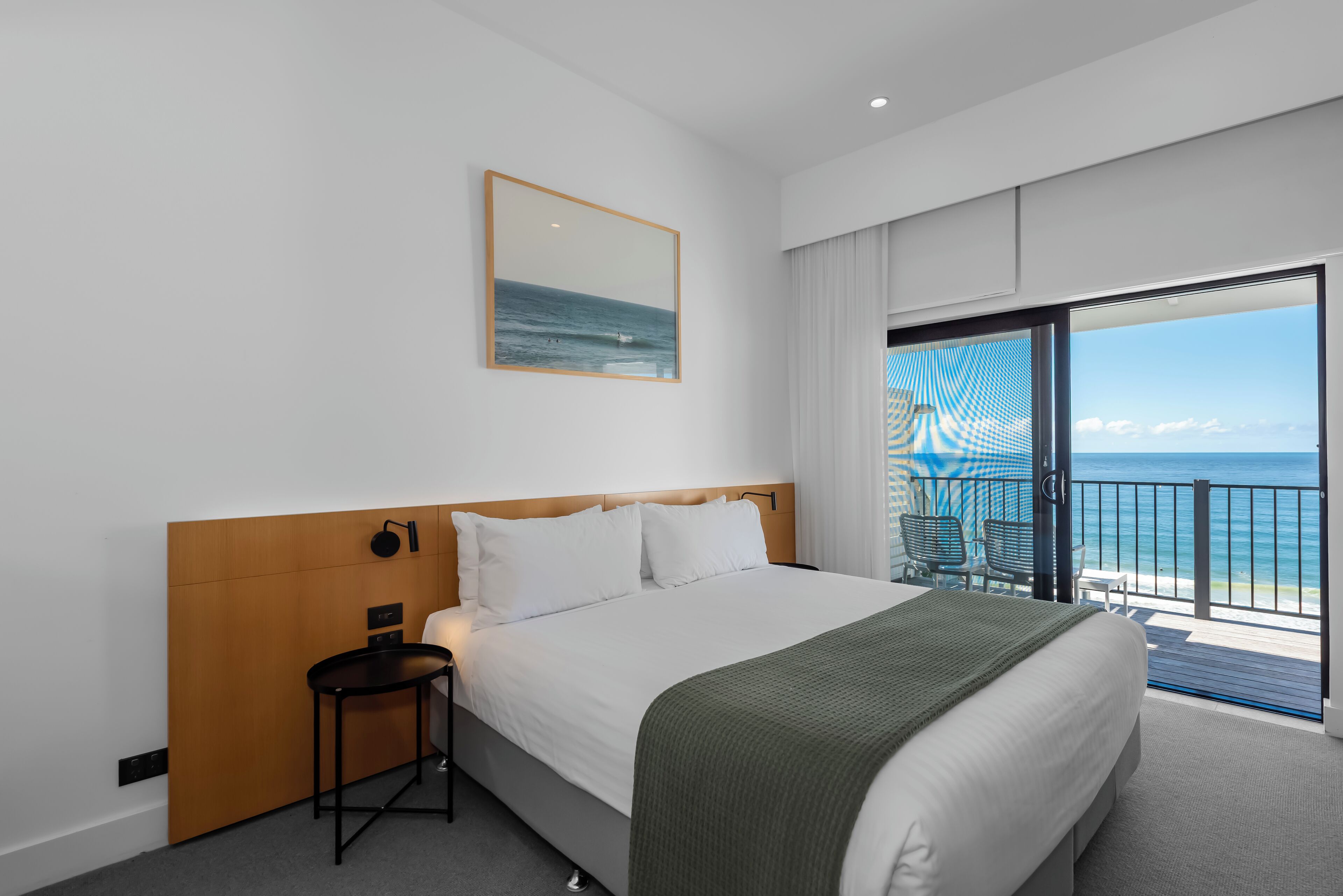 Een hotelkamer met een groot bed, een tafeltje, een stoel en een balkon met uitzicht op de oceaan.