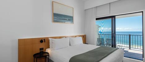 Et hotelværelse med en stor seng, et lille bord, en stol og en balkon med havudsigt.