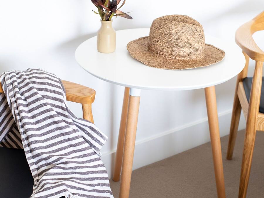 Una habitación con una mesa redonda blanca, un sombrero de paja, una manta a rayas y una pequeña planta sobre la mesa.