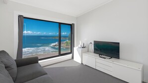 A modern living room with a large window offering a view of the ocean and a white entertainment unit with a flat-screen TV. - Pacific Hotel Yamba (Yamba)