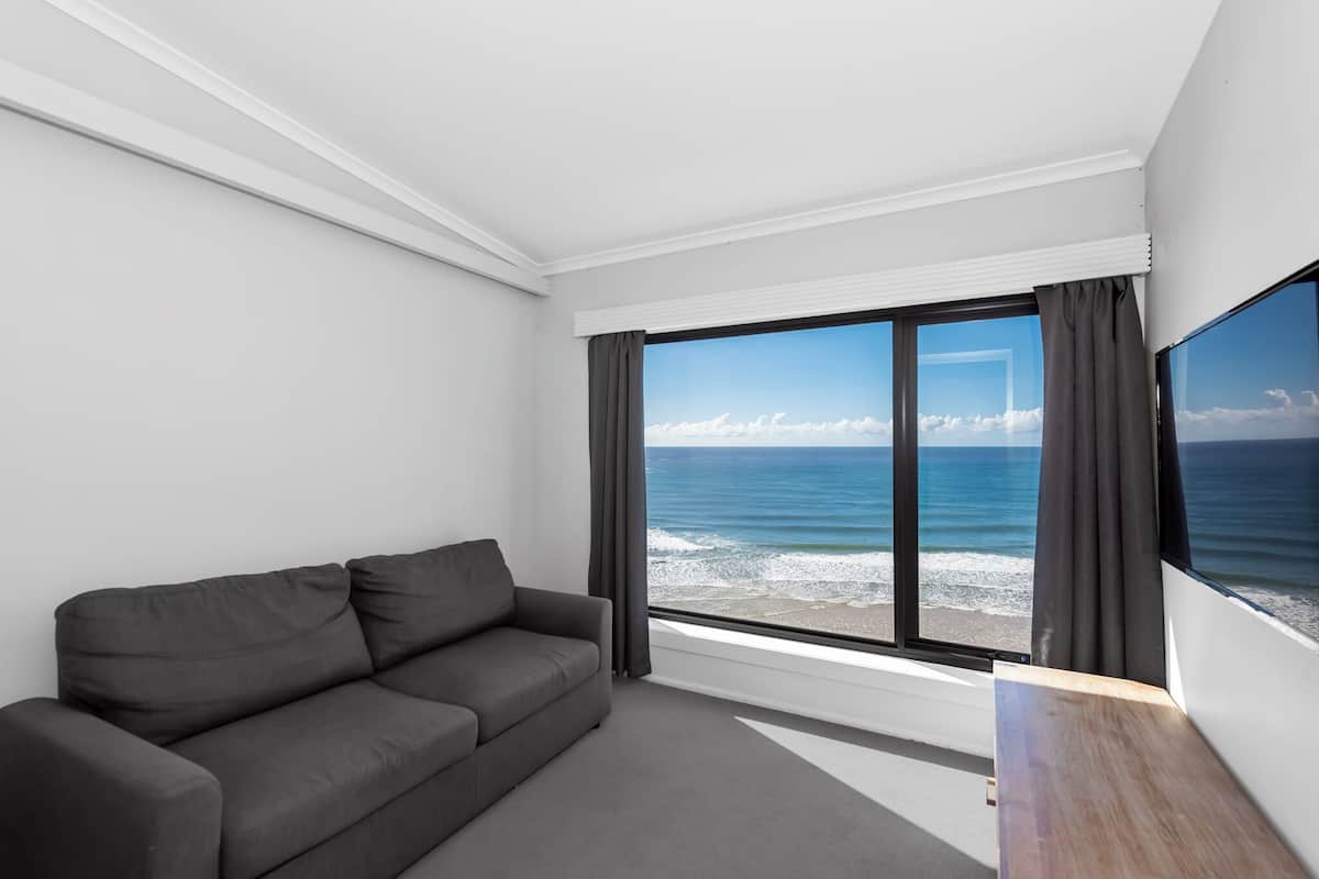 A modern room with a grey sofa, large windows with curtains, and a flat-screen TV.