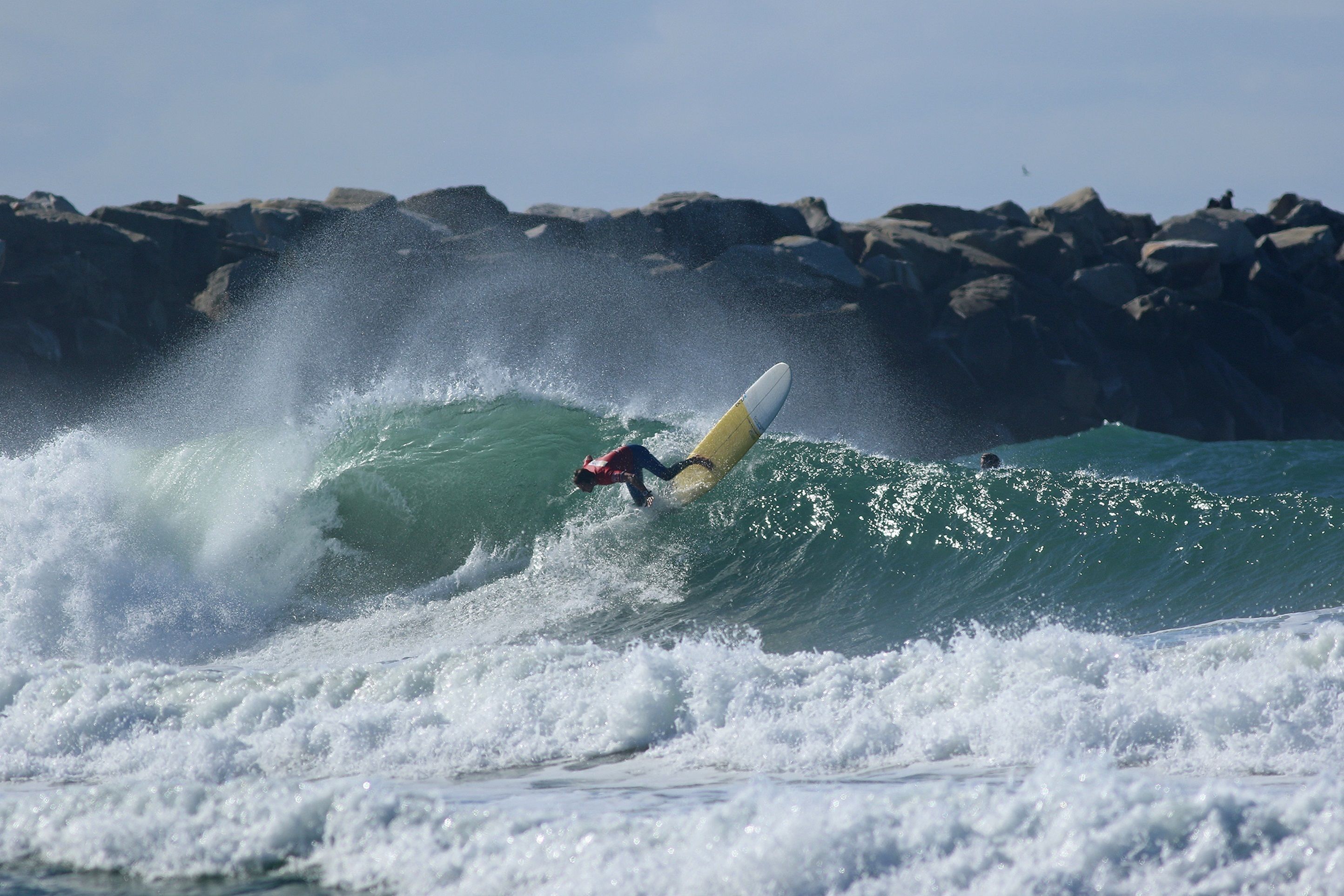 Un surfista montando una ola, con una costa rocosa al fondo.