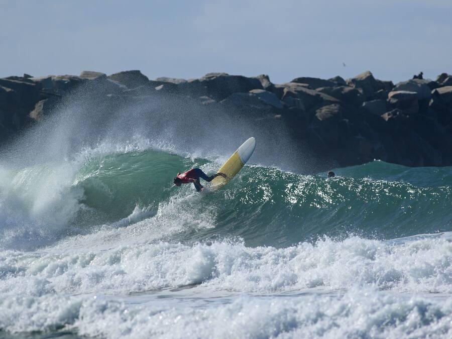 Un surfista montando una ola, con una costa rocosa al fondo.