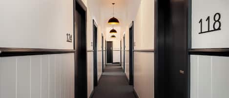 A hotel hallway with black and white walls, numbered doors, and pendant lighting.