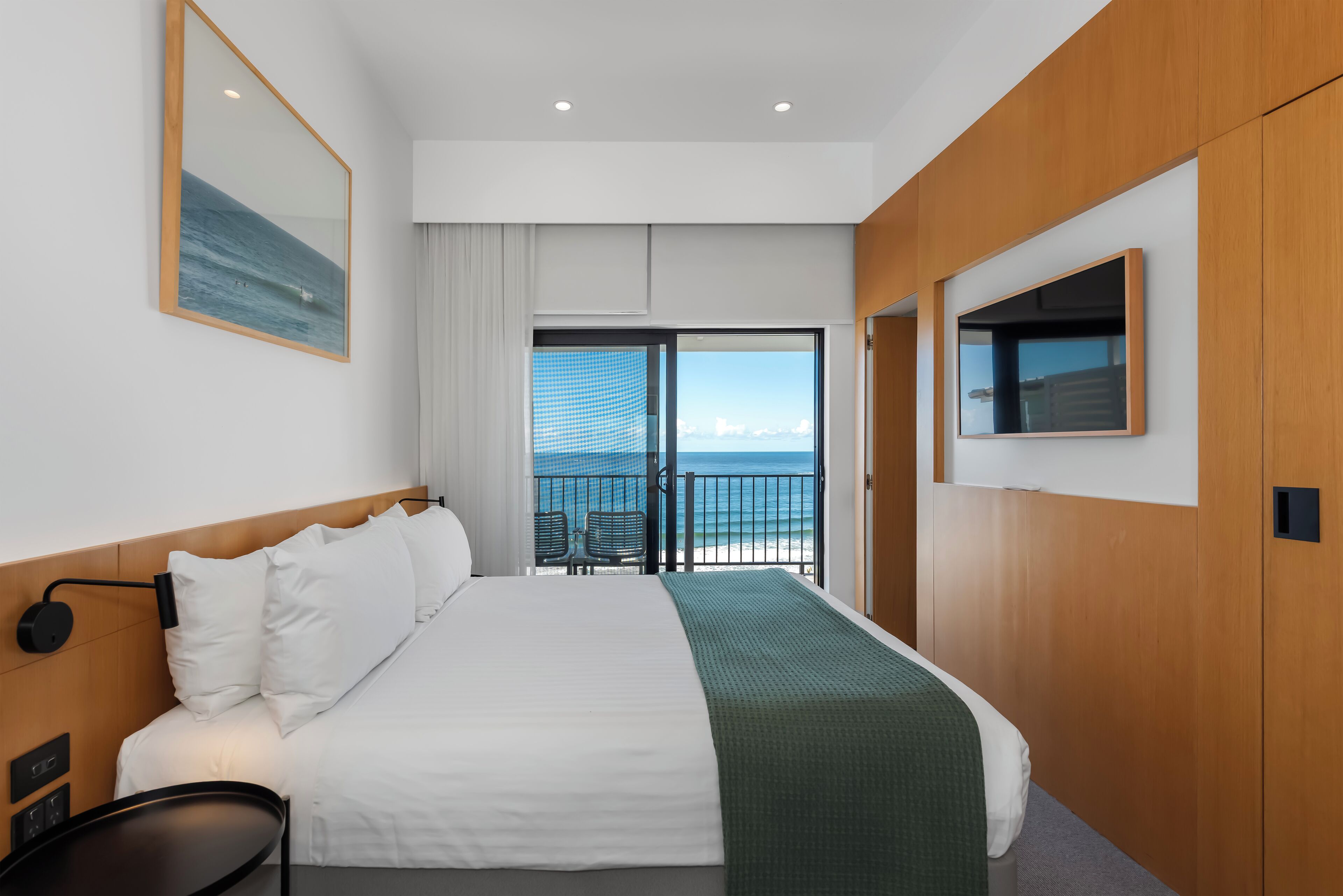 Habitación de hotel con una cama grande, televisión, balcón con vista al océano y un panel de pared de madera.
