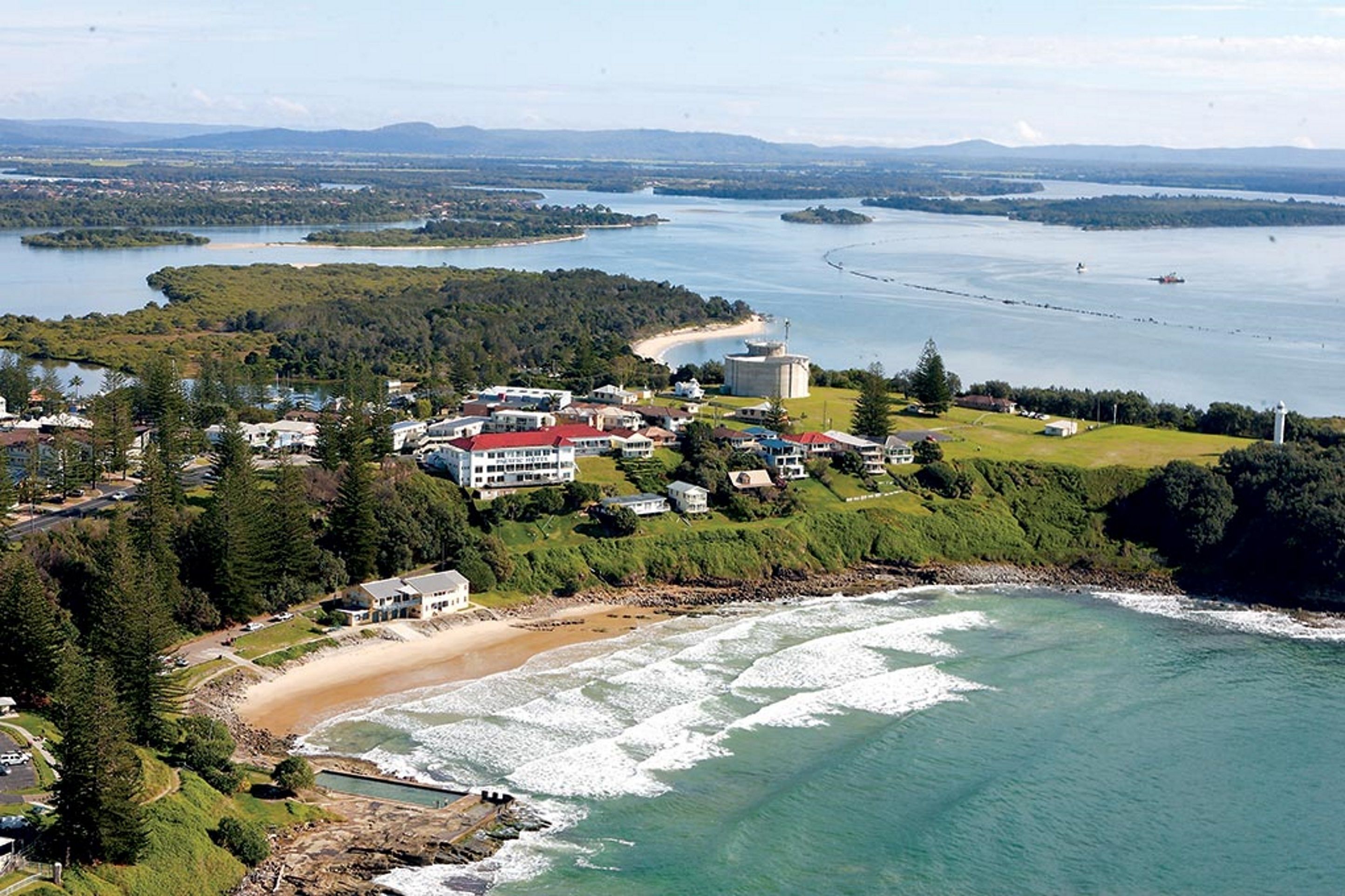 An aerial view of a coastal town with a beach, houses, and a lighthouse.