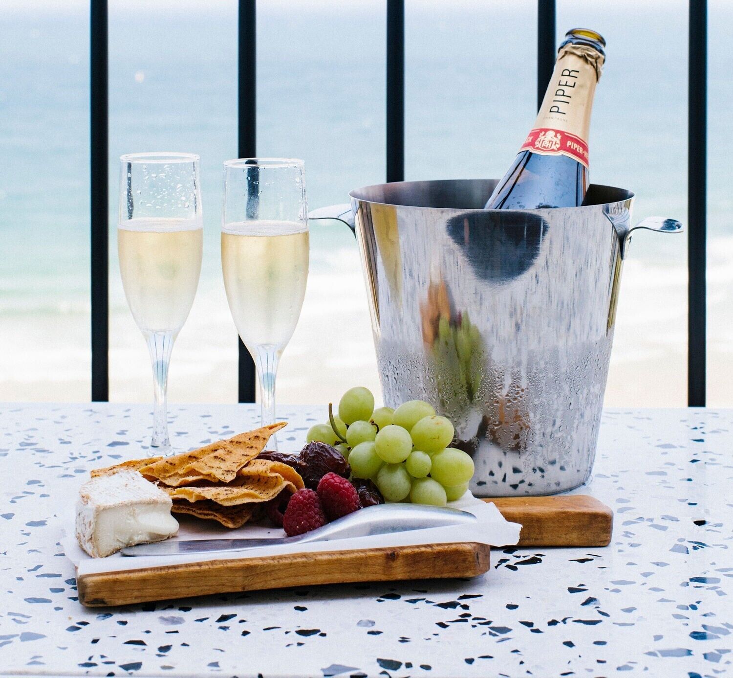 A table with a bottle of champagne, two glasses, and a variety of snacks and fruits.