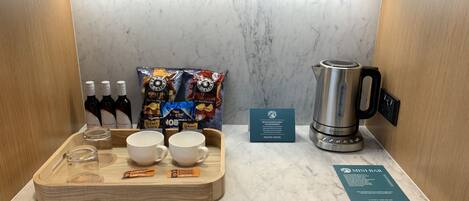 A breakfast setup with a tray of coffee cups, a kettle, and food packets on a marble countertop.