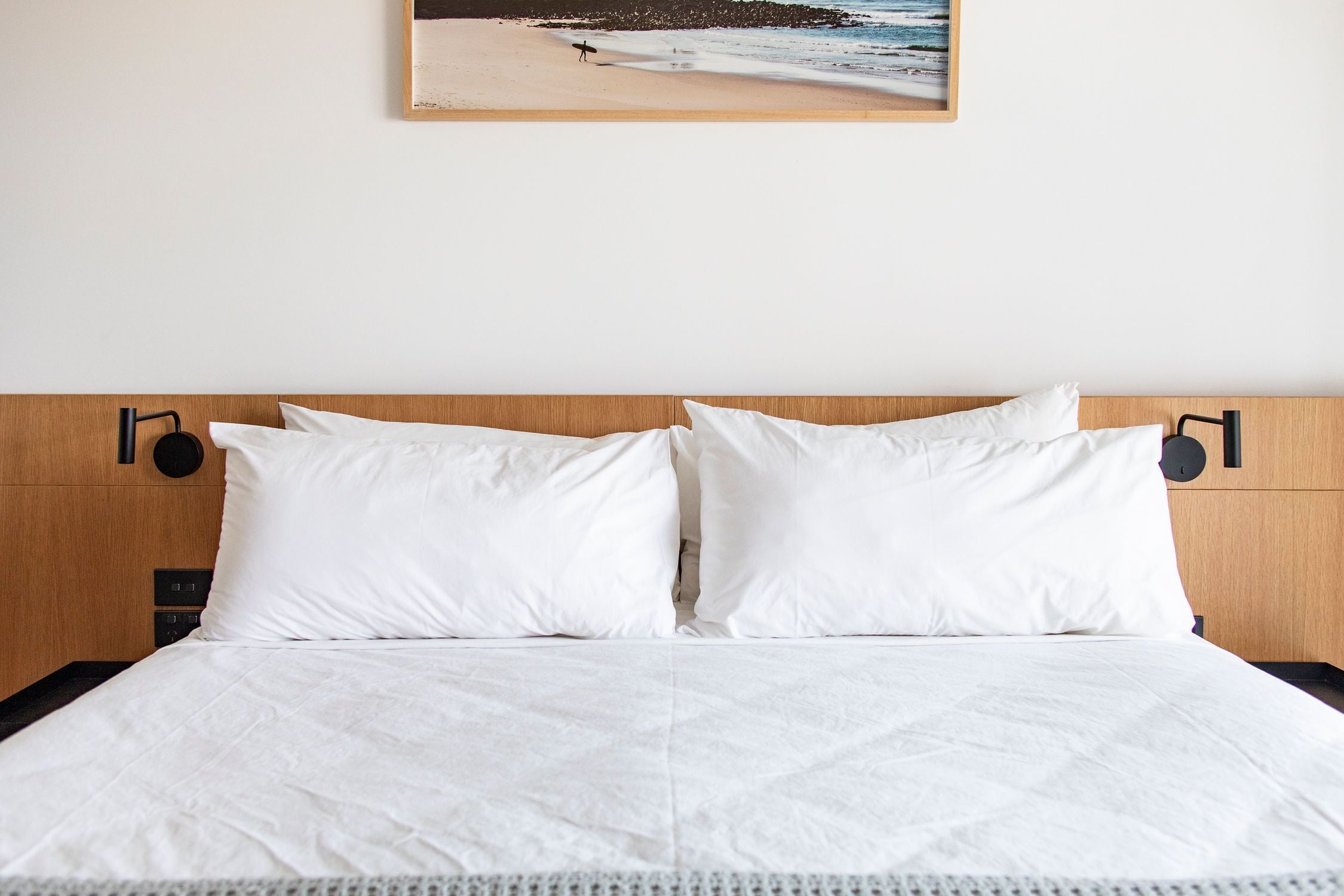A neatly made bed with white linens and a wooden headboard.