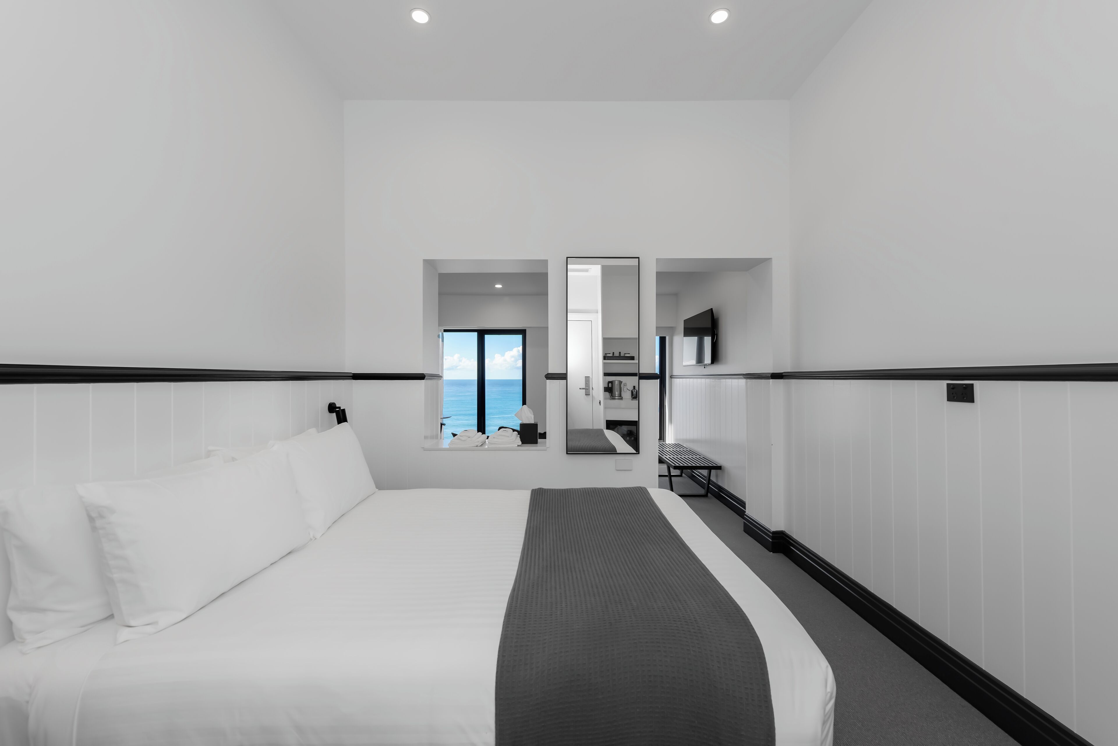 A modern hotel room with a large bed, a view of the sea, and a separate bathroom area.