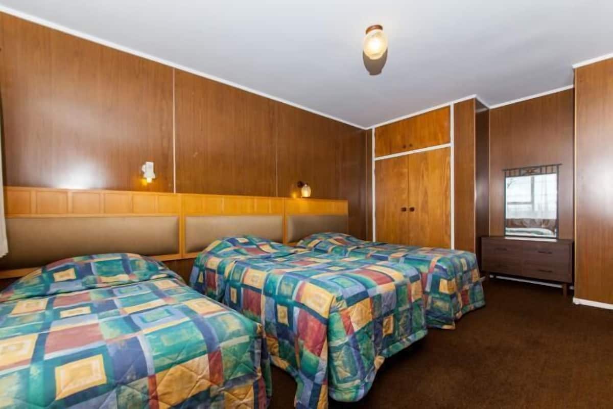 Habitación de hotel con dos camas, paneles de madera, un aparador y una ventana.
