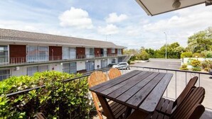 A balcony with a wooden table and chairs, overlooking a building with a tiled roof and a parking area. - Sunset Lodge Motel (Auckland)