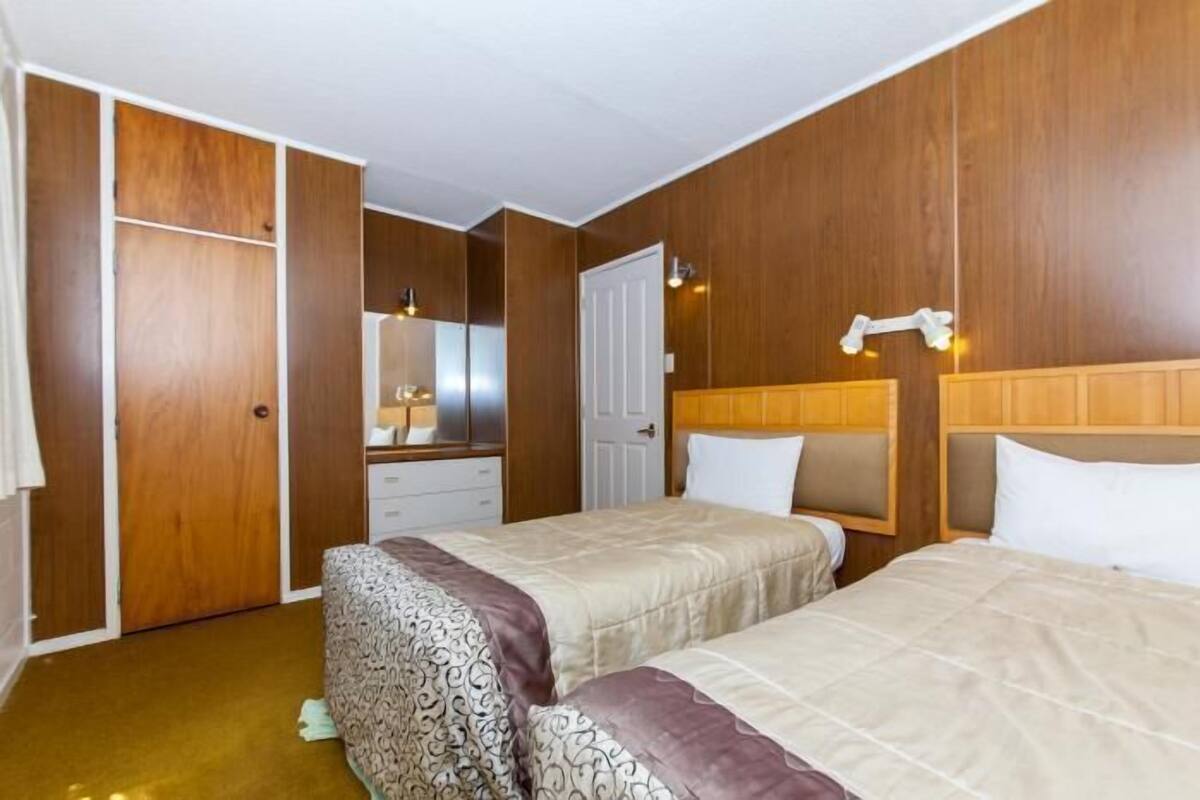 Habitación de hotel con dos camas, paneles de madera, un armario, un espejo y una mesita de noche.