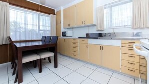 A modern kitchen with beige cabinets, a dining table with chairs, and a large window with curtains. - Sunset Lodge Motel (Auckland)