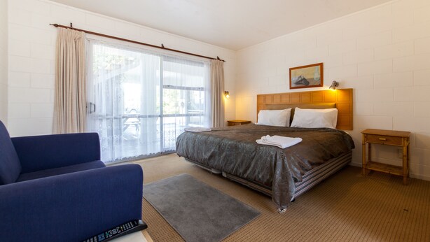 A hotel room with a bed, a sofa, a small table, and a window with curtains. - Sunset Lodge Motel (Auckland)